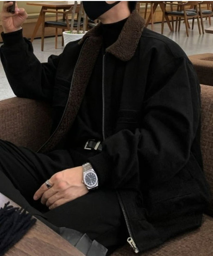 カフェのソファに深く腰掛ける男性のクローズアップカット。袖口のリブから覗くシルバーのメタルウォッチ（腕時計）と、マットなボディ生地のコントラストがラグジュアリーな雰囲気を演出。