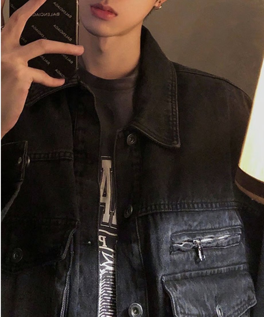 スマートフォンの画面を鏡に向けて撮影した上半身のミラーセルフィー。ジャケットのフロントボタンを開け、インナーのカレッジ風グラフィックTシャツを覗かせた、ラフで男らしい着こなし。