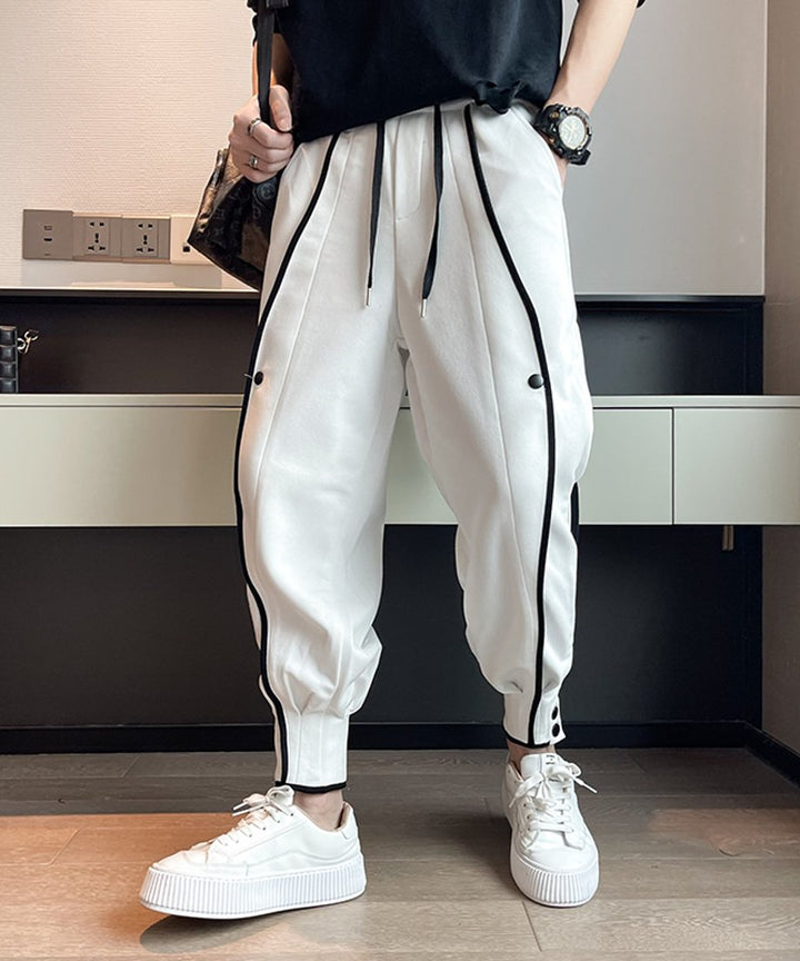 黒のラインとボタンが映えるホワイトのスウェットジョガーパンツを穿き、黒Tシャツを合わせた男性のフロントカット。