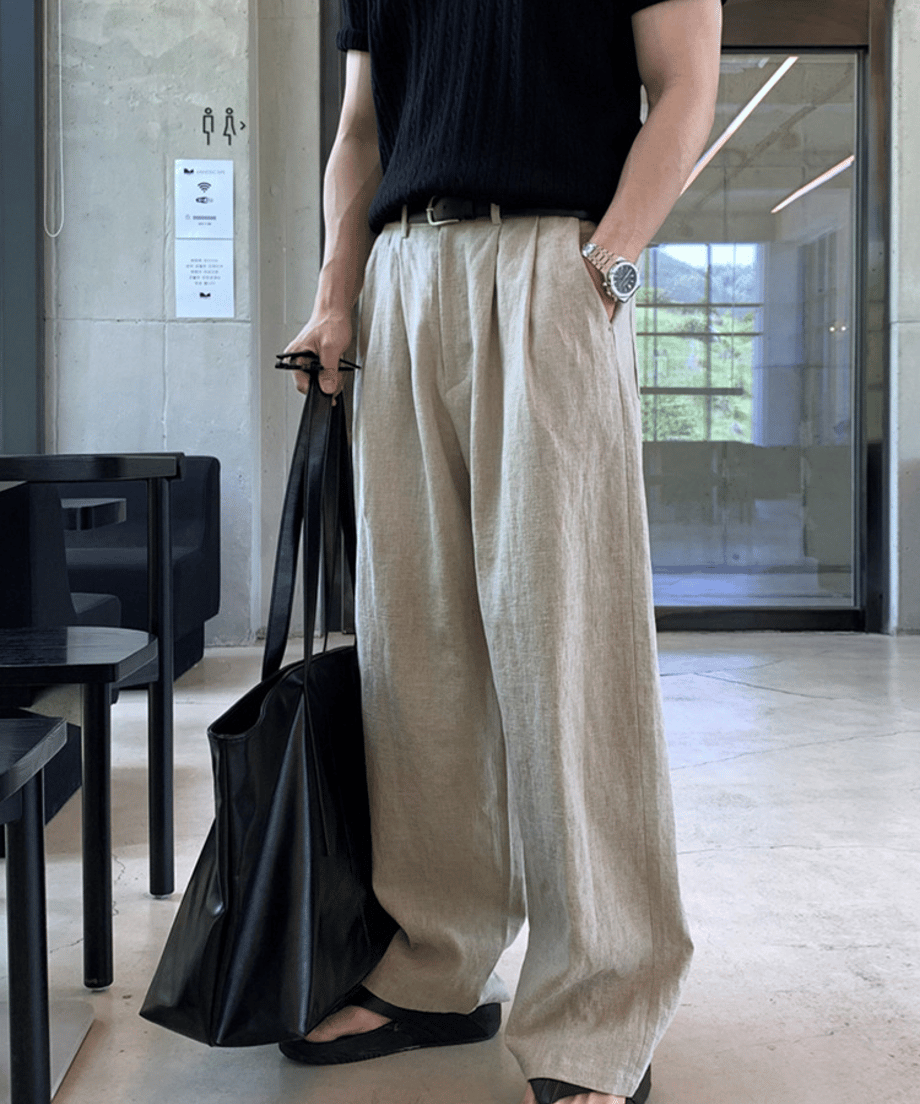 ベージュのリネン混ワイドパンツに黒の半袖ニットとレザーベルトを合わせ、黒いトートバッグを手にした男性のフロントカット。