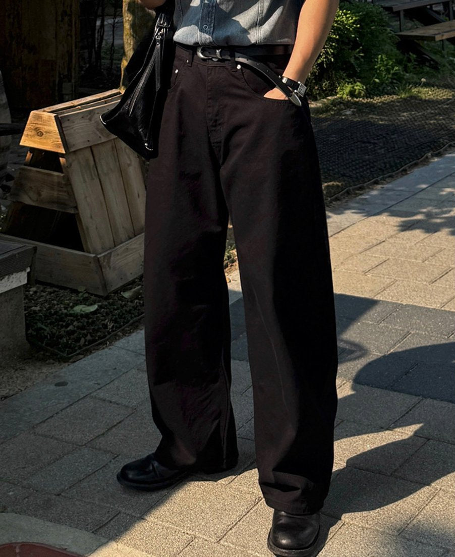 黒のワイドストレートパンツのフロントに焦点を当て、ポケットに手を入れた男性の腰元・足元のアップカット。