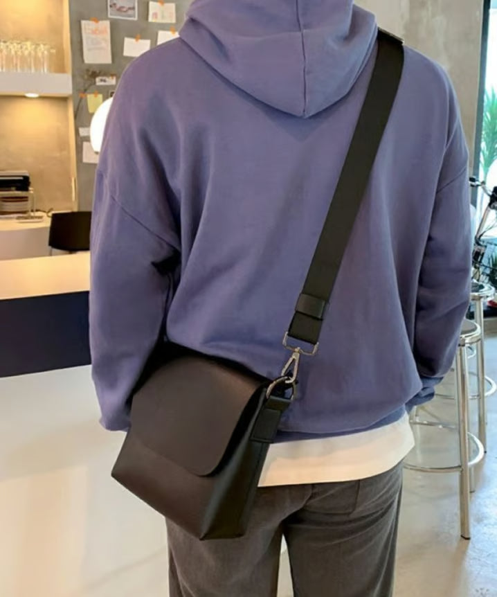 パーカースタイルの人物がブラックのフラップショルダーバッグを斜め掛けしたバックスタイル。